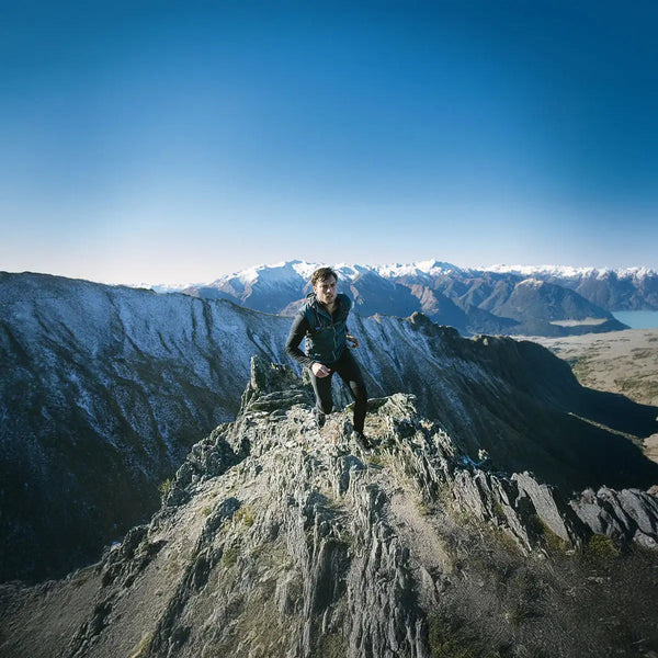 Eine Person auf einem Berggipfel und im Hintergrund verschneite Berge.